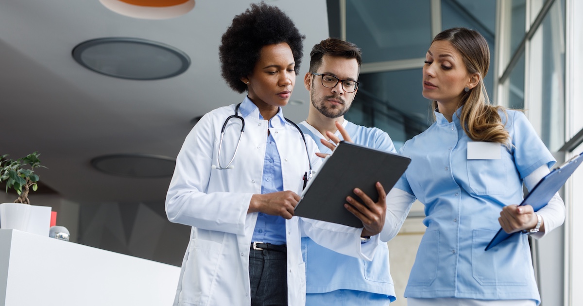 
  Three healthcare providers standing next to each other and looking at a tablet
