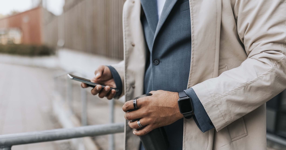 
  Midsection of a person in a suite wearing two rings and looking at their phone
