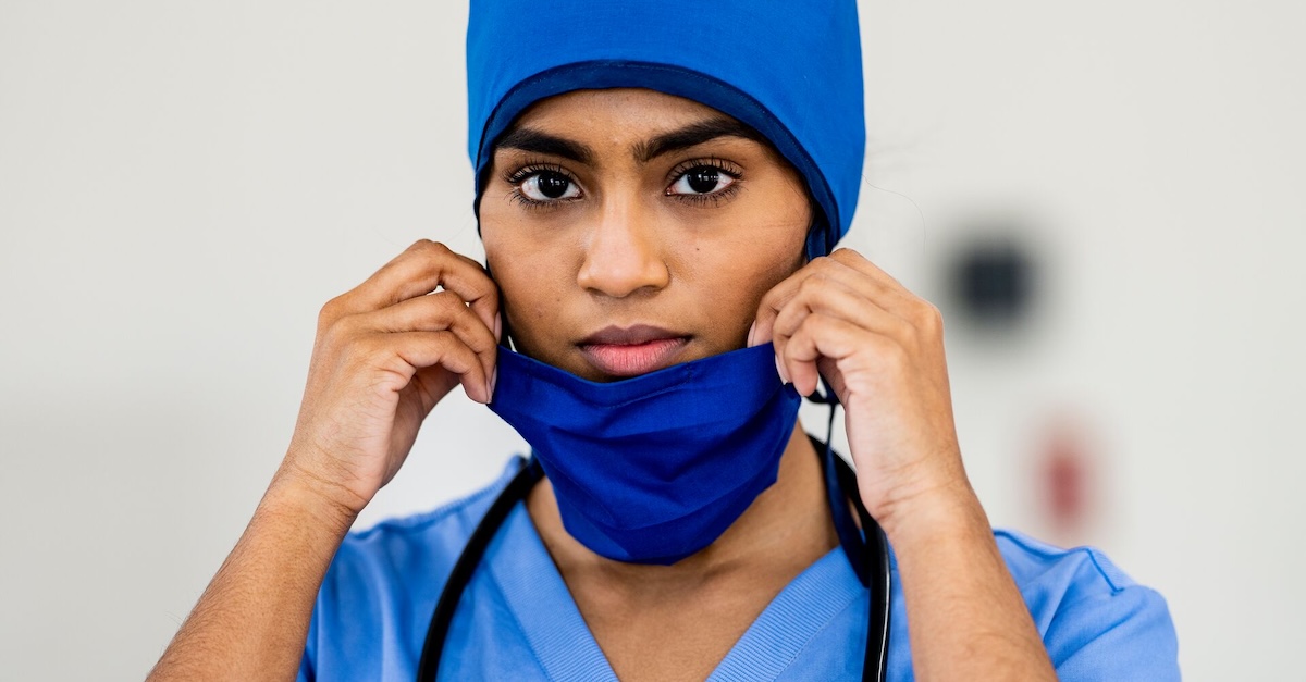 
  Doctor wearing blue scrubs and holding their face mask
