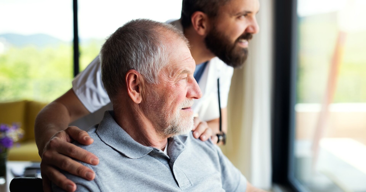 
  Person sitting in a chair while looking out a window with another person standing beside them
