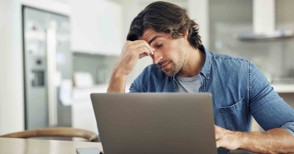 Stressed person sitting at a computer with their head in their hand