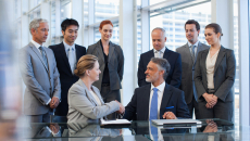 Two people shaking hands with others standing around watching