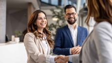 Two people shaking hands while another person watches