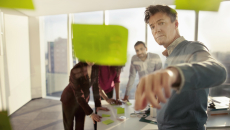 Numerous people standing in a room and looking at post-its on a wall