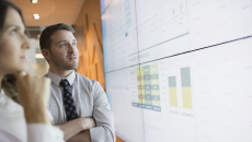 Two people standing in front of a large white board that has graphs on it