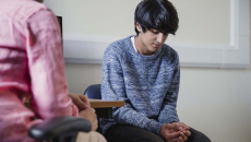 Two people sitting in a room, one with their head down