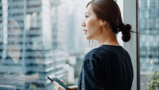 Person standing up while holding a phone and looking out a window