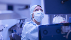 Healthcare provider wearing scrubs and a face mask while looking at a computer screen