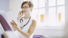 Healthcare provider sitting down in a clinicak setting while looking at a tablet