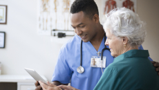 Healthcare professional standing next to a patient while holding a tablet