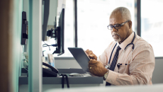 Physician sitting at their desk while looking at a tablet