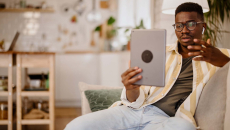 Person sitting on the couch in a home while holding up a tablet in front of them