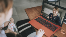 Two people sitting on a couch while looking at an orange and black computer and speaking with a virtual healthcare provider