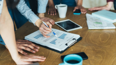 A close up of businesspeople gathered around a table looking at financial charts