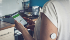 Woman checking glucose level with a remote sensor and mobile phone.