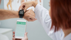 A doctor helping a patient synchronize heart rate data on a smart watch and phone