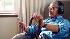 An older man wearing headphones looking at a smartphone