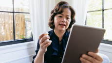 An older woman holding a pill bottle talking to a provider using her tablet.