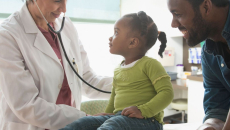 Healthcare provider and another adult standing by a child on an exam table