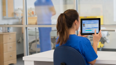 Healthcare provider in the clinical setting sitting at a desk and looking at a tablet