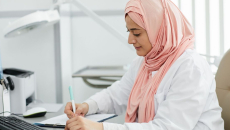 A nurse wearing a hijab filing a patient's form at a desk