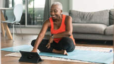 A woman sitting on a yoga mat using a tablet