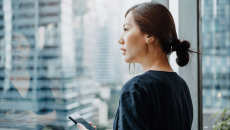 A person holding a smartphone looking out a window.