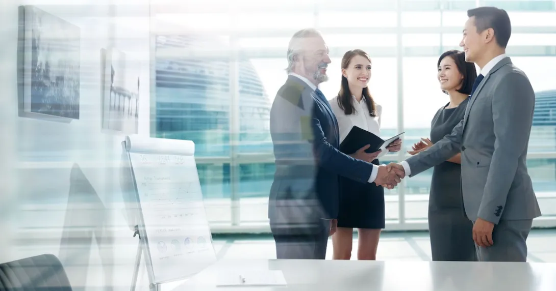 Four people standing in a room with two of them shaking hands
Four people standing in a room with two of them shaking hands