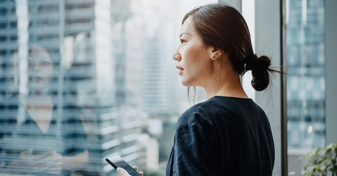 A person holding a smart phone looking out the window