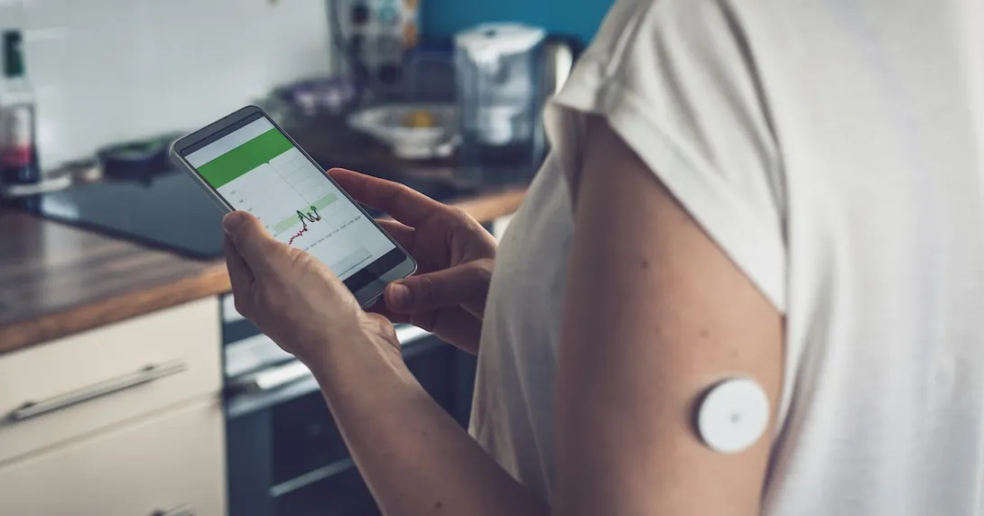 Person wearing CGM patch tracks data on mobile app