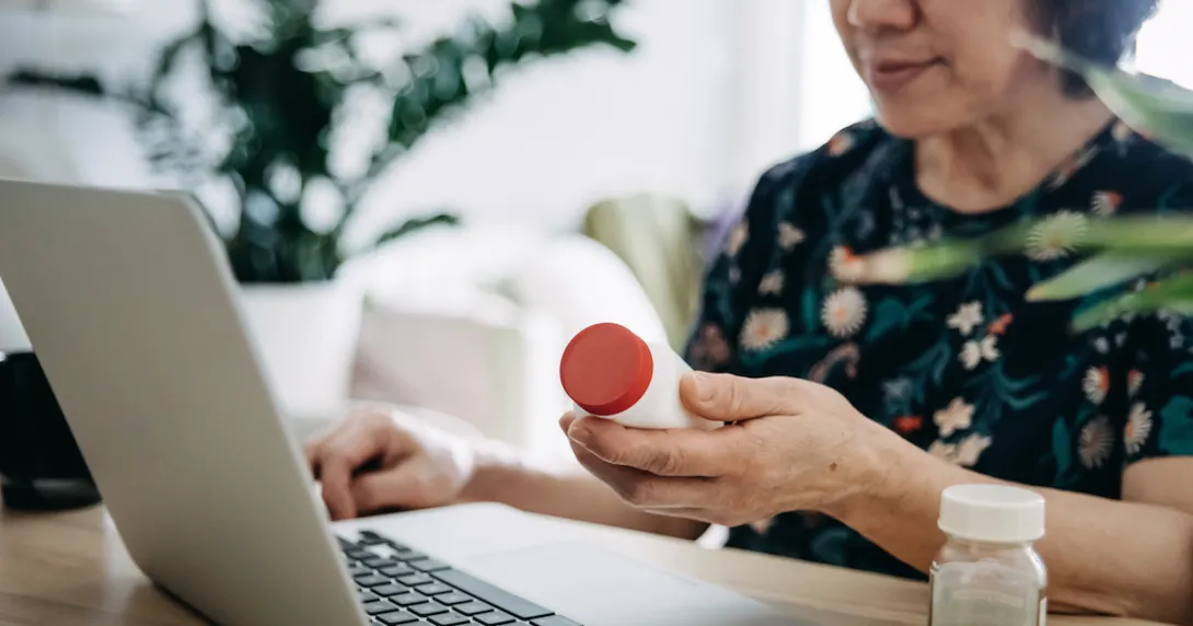 Person holding a pill bottle while sitting and looking at a computer