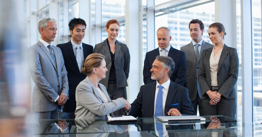 Two people shaking hands with others standing around watching