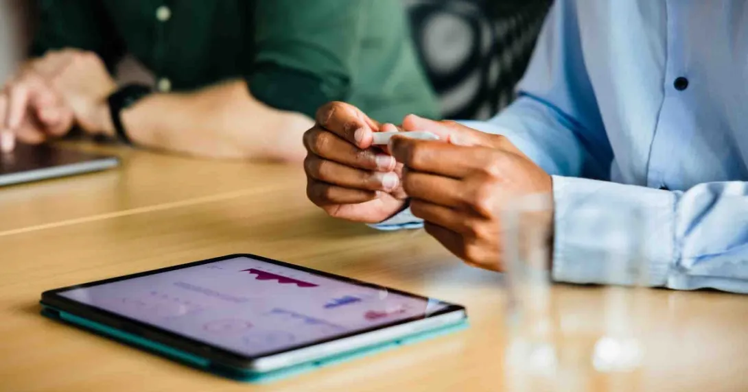 Two people sitting at a desk with a tablet on it