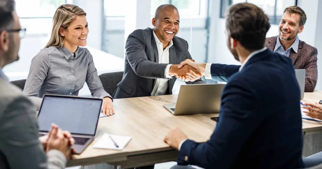 People sitting across from each other at a table and shaking hands