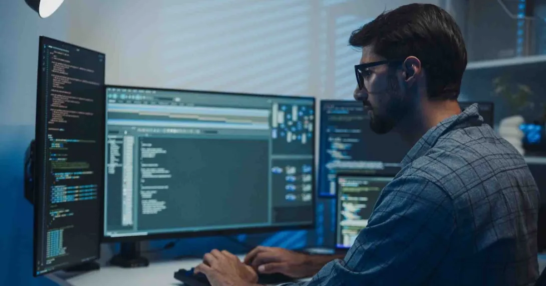 Developer sitting at a desk and looking at numerous screens on a computer
