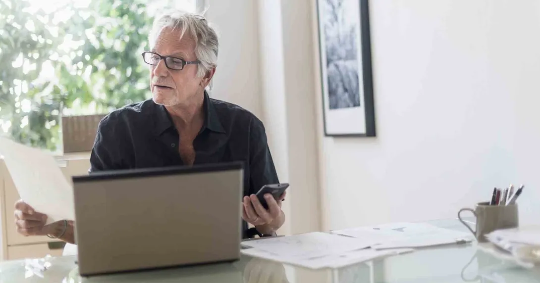 Person sitting in their home office while looking at a computer and a piece of paper