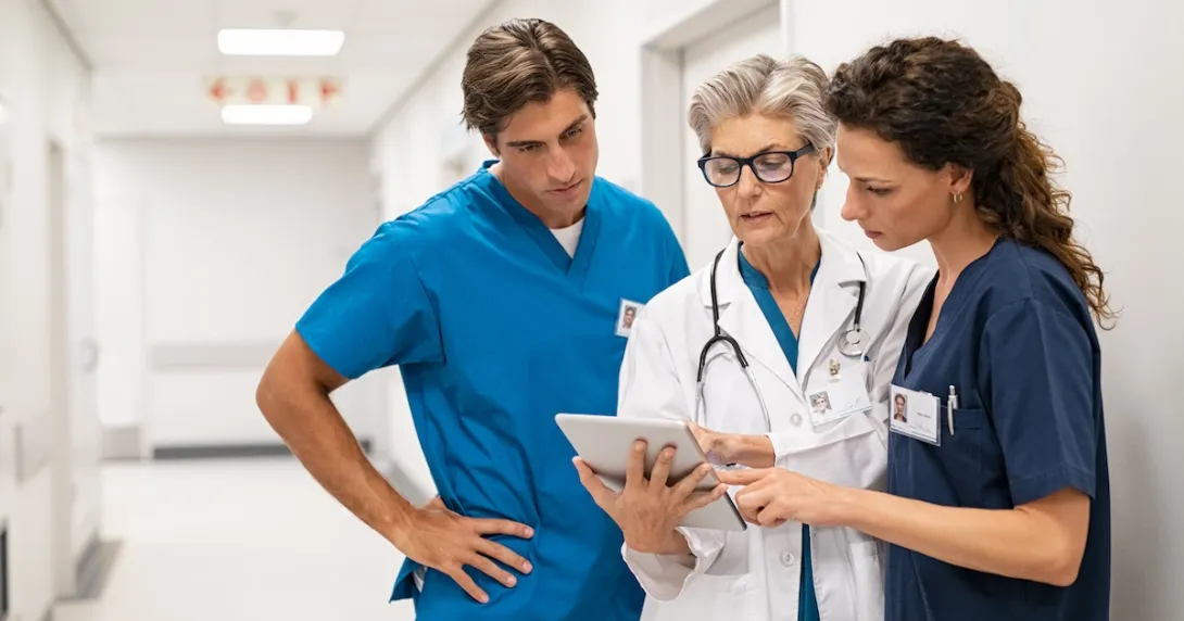 Three healthcare providers standing in the hallway of a hospital while looking at a tablet