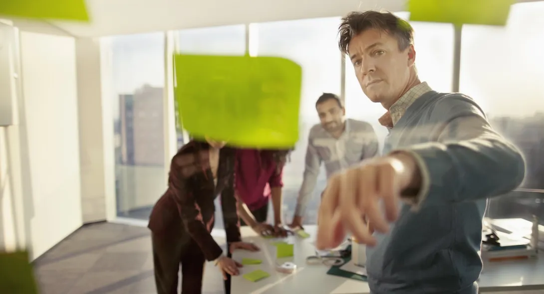 Numerous people standing in a room and looking at post-its on a wall