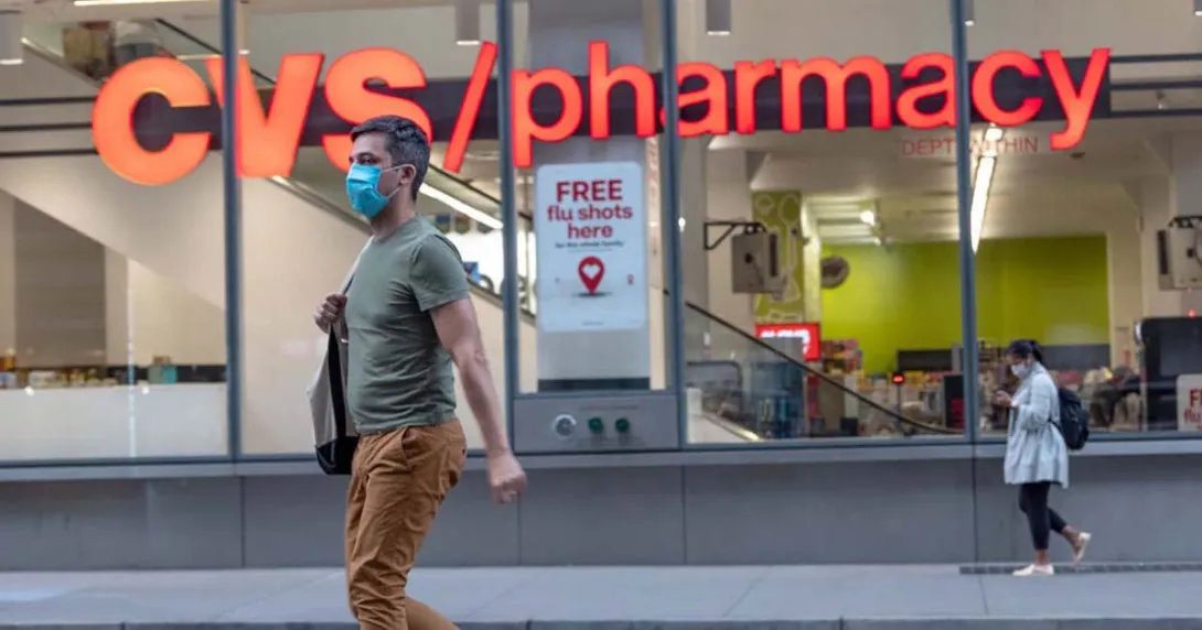 A masked person walking by a CVS pharmacy.