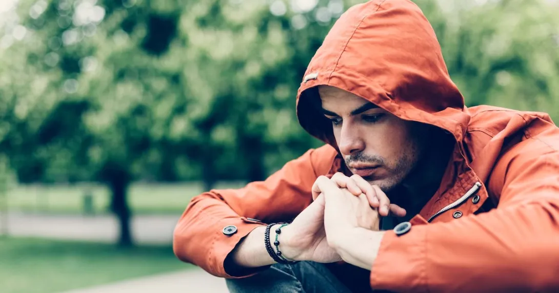 Person sitting in a park while wearing an orange sweater with a hood