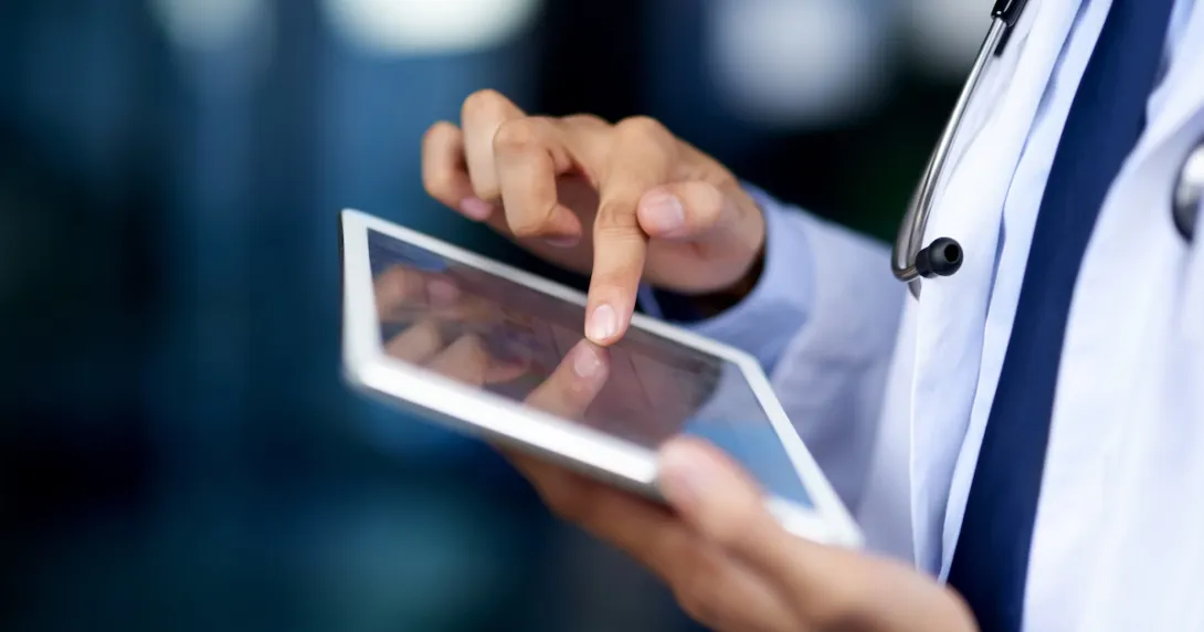 Healthcare provider holding a tablet while wearing a lab coat and stethoscope