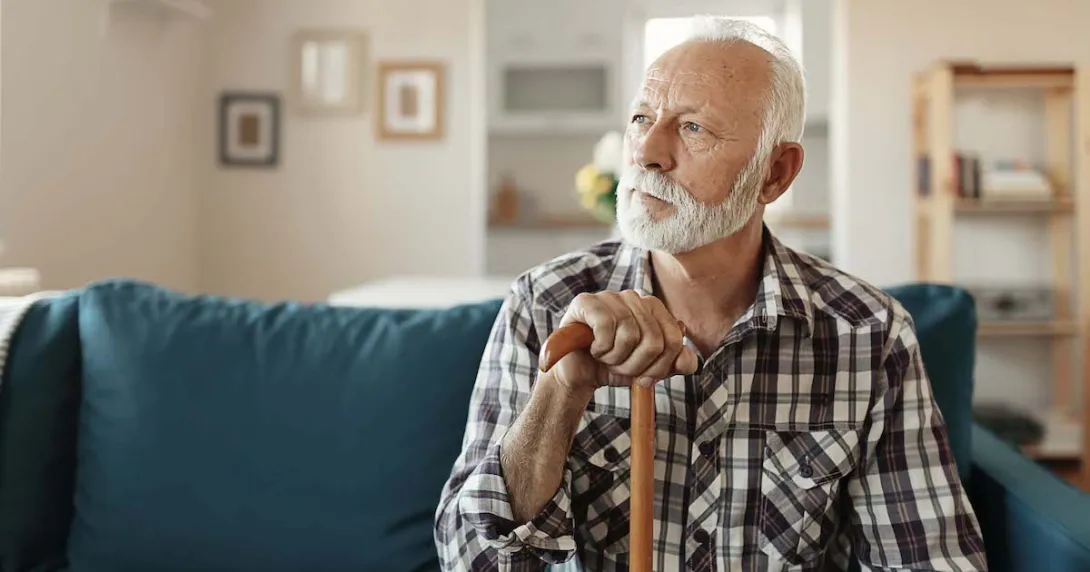 Person sitting on a couch looking away from the camera while holding a wooden cane