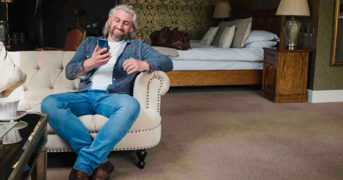 Person sitting on the couch in a hotel room smiling and looking at their phone