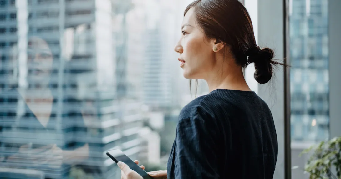 Person looking out the window while holding a mobile phone