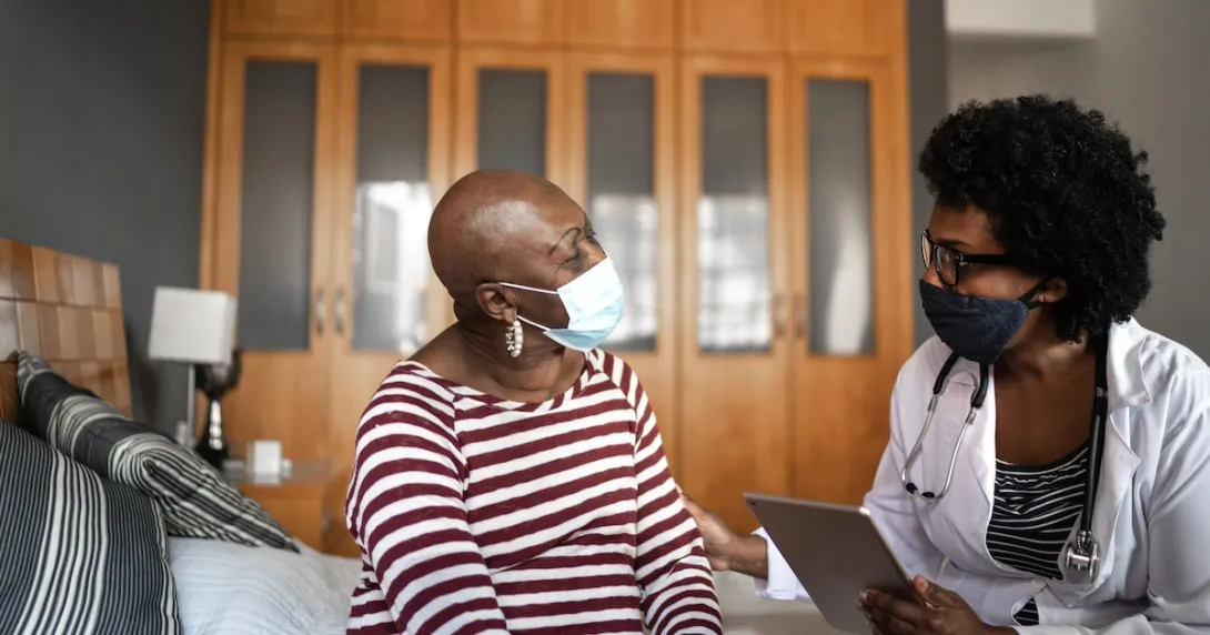 Two individuals sitting in a home looking at each other while wearing face masks