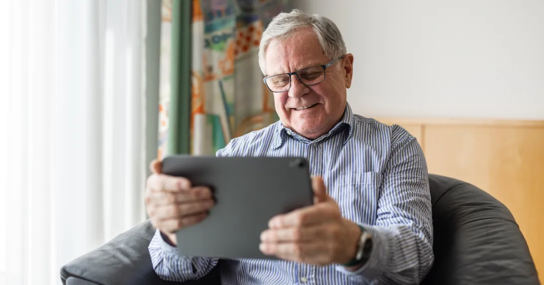 Person sitting in a chair smiling while looking at a tablet