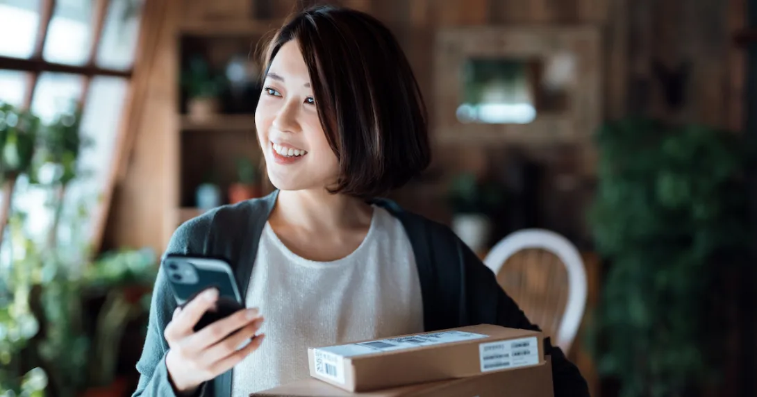 Person standing in a house holding a phone with a box in front of them
