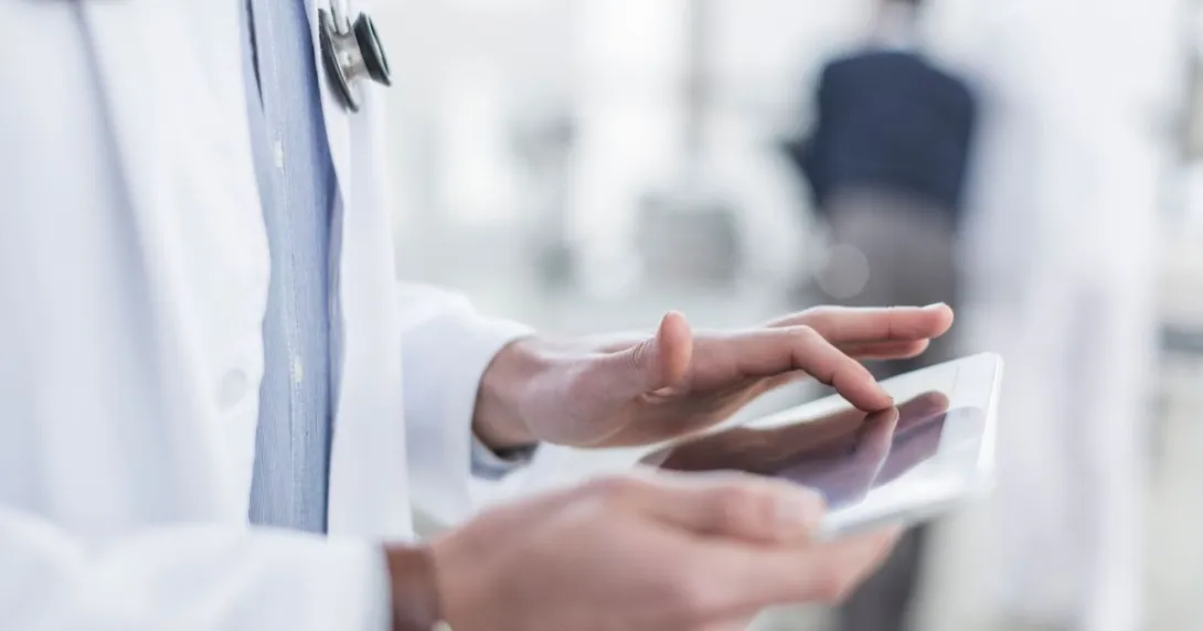 The body of a healthcare provider using a tablet while wearing a lab coat and stethoscope around their neck