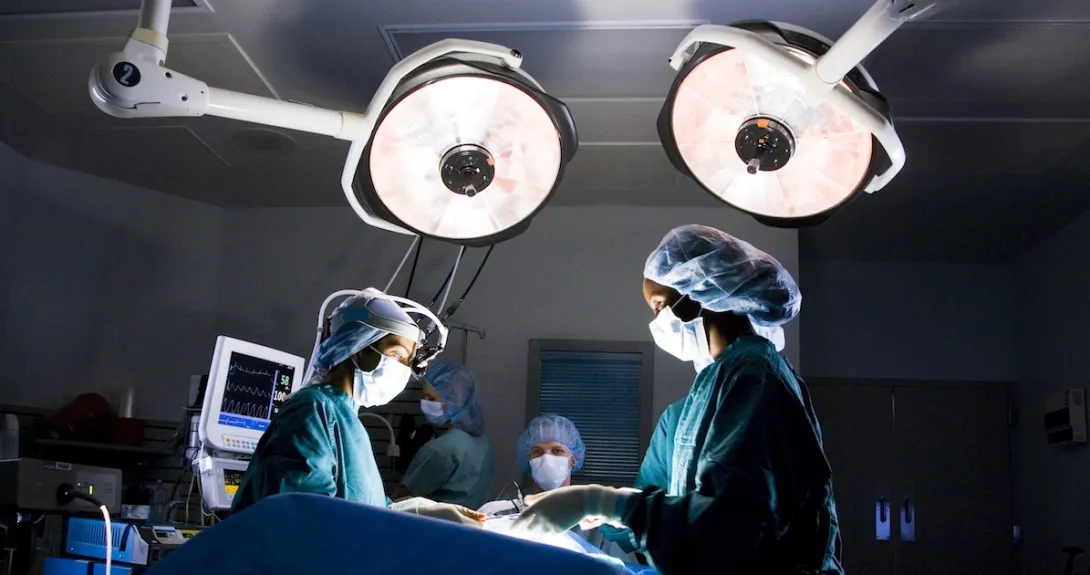 Healthcare providers performing surgery on a patient with lights shining down from the ceiling