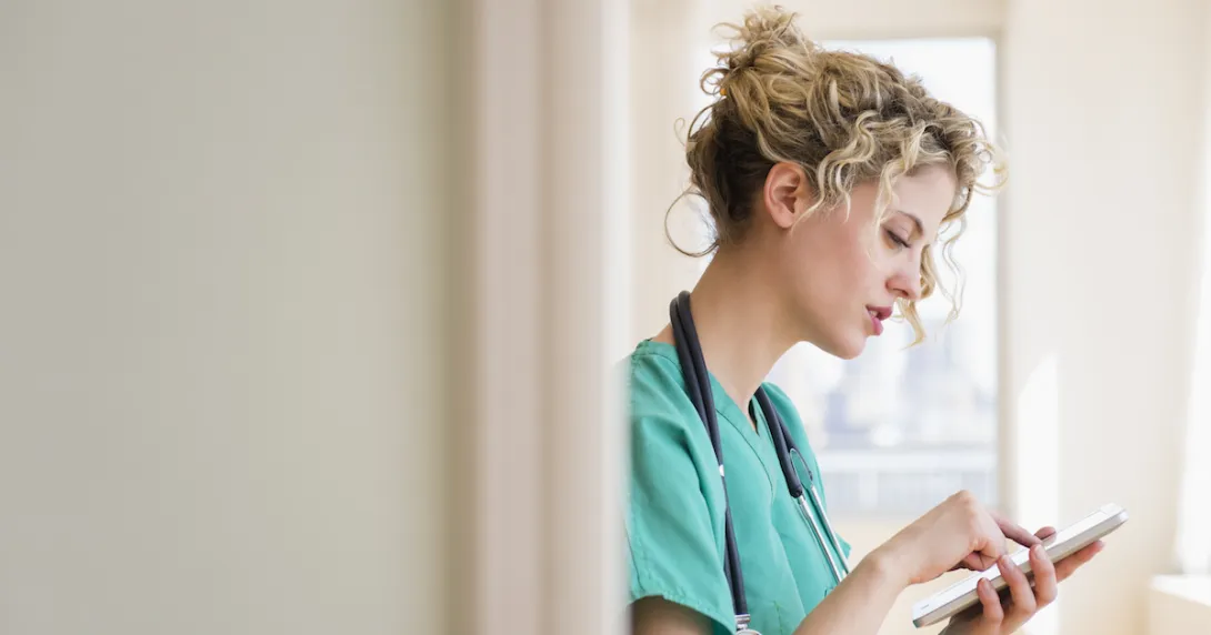 Nurse standing in a hallway while looking at a tablet